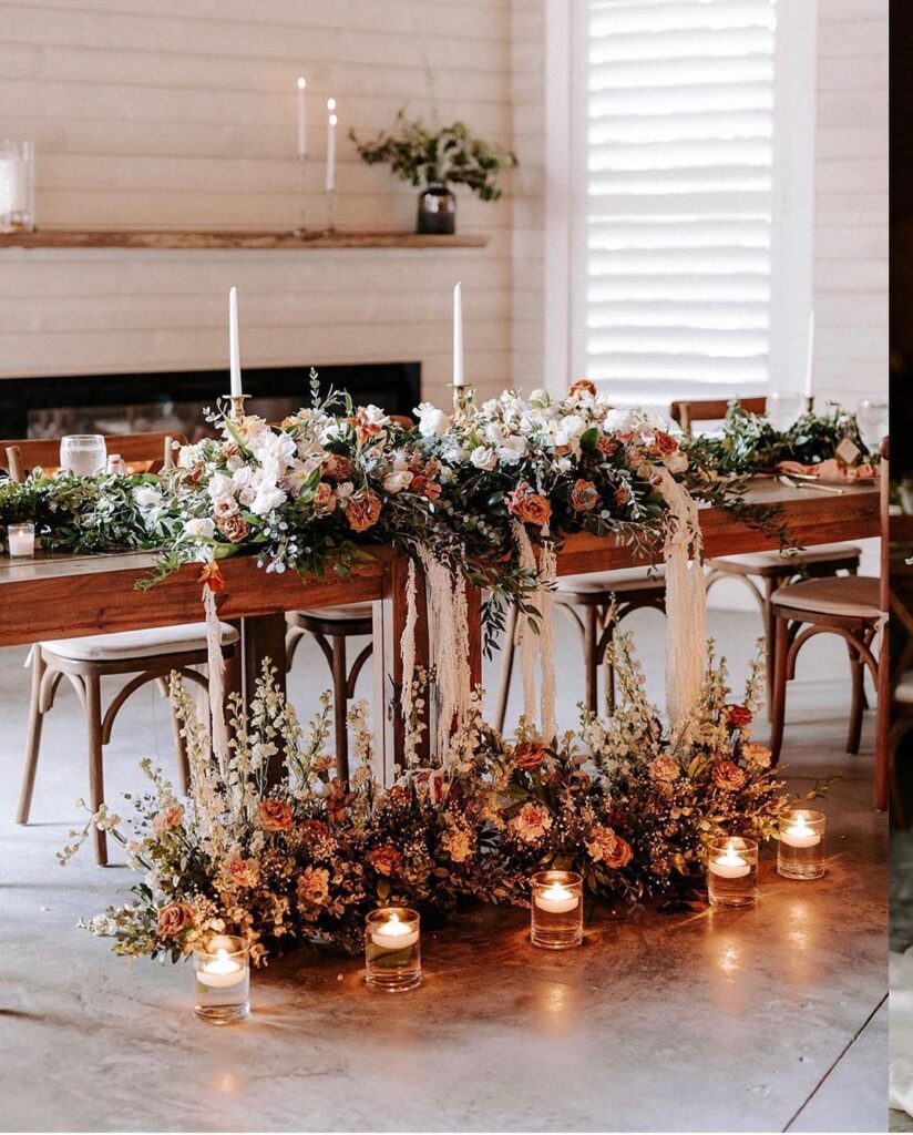 wooden table with lush floral garlands and variety of candles with fireplace and mantle in background